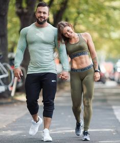 a man and woman walking down the street holding hands while wearing sports bra tops, tights and leggings