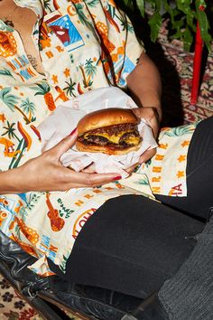 a woman sitting on a chair holding a hamburger in her hand and wearing black pants