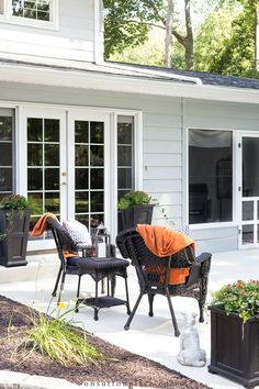 an outdoor patio area with chairs and plants on the side of the house that is painted white