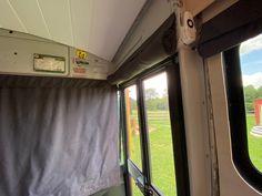 the inside of an rv with windows and curtains on it's sides, looking out onto a grassy field