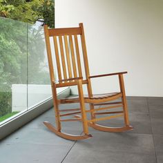 a wooden rocking chair sitting on top of a cement floor next to a large window