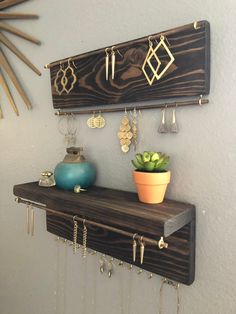 a wooden shelf with earrings hanging from it's sides and a potted plant on top