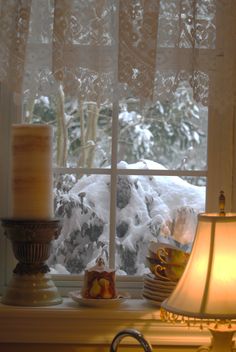 a window sill covered in snow next to a lit candle and some dishes on the windowsill