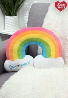 a rainbow pillow sitting on top of a gray couch next to a white teddy bear