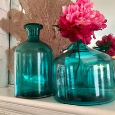 two blue vases with pink flowers in them sitting on a mantle next to a mirror