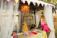 a table covered in food under a canopy with white drapes and pink flowers on it