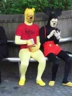 three people in costumes sitting on a bench with one person wearing a mask and the other holding a cell phone