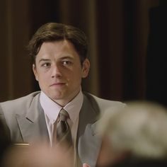 a man in a suit and tie sitting at a table with other people around him