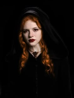 a woman with long red hair wearing a black hoodie and dark makeup is looking at the camera