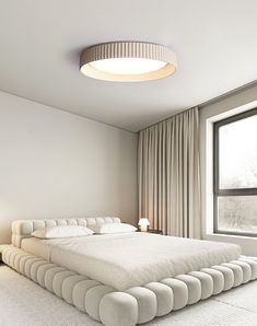 a large white bed sitting next to a window in a bedroom under a round light fixture