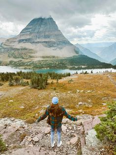 a woman standing on top of a rocky hill next to a lake and mountain range