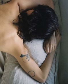 a woman laying on top of a bed with her arm around the back of her head