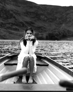 a woman sitting on the bow of a boat with her hands behind her head, in front of mountains