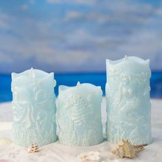 three frosted candles sitting on top of a sandy beach next to shells and seashells