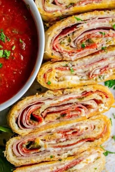 several sandwiches with meat and tomato sauce on them next to a bowl of dipping sauce