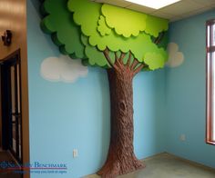 a room with a tree painted on the wall and a teddy bear sitting under it