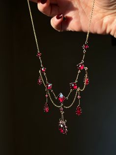 a woman's hand is holding a necklace with red stones and gold chains on it