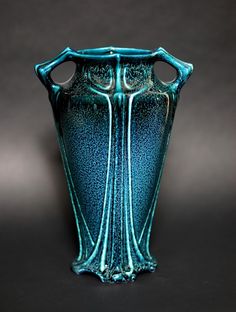 a blue glass vase sitting on top of a table next to a black wall and floor