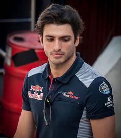 a man wearing a polo shirt and looking at the camera while standing in front of a red barrel