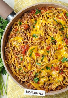 a skillet filled with spaghetti, meat and cheese on top of a table next to parsley