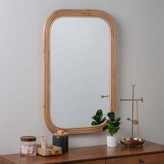 a mirror sitting on top of a wooden dresser next to a potted plant and candle