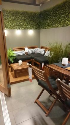 an outdoor seating area with wooden furniture and plants on the wall behind it, in front of a sliding glass door