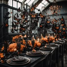 a dining table set with black and orange plates, silverware and butterflies hanging from the ceiling