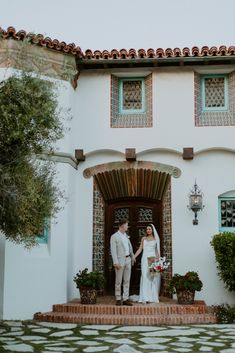 a bride and groom standing in front of a house