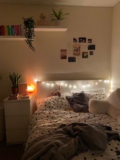 an unmade bed with lights on the headboard