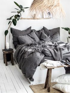 a bed with grey linens and pillows in a white room next to a potted plant