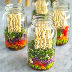 four mason jars filled with noodles and vegetables