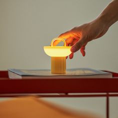 a hand reaching for a yellow basket on top of a wooden table with a red chair in the background