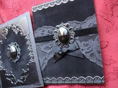 two black and silver wedding cards on a pink tablecloth with lace, bows and jewels