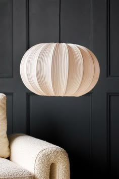 a white chair sitting in front of a black wall with a light fixture hanging from the ceiling