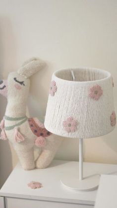 a stuffed animal sitting next to a lamp on a white dresser with pink flowered lampshade