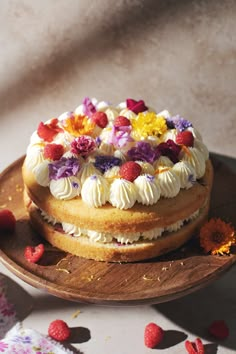 a cake with white frosting and colorful flowers on top sitting on a wooden plate