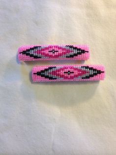 two pink and black beaded hair clips sitting on top of a white cloth covered table