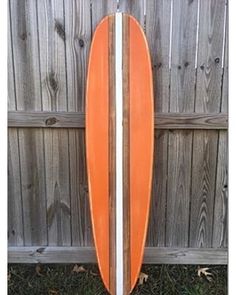 an orange and white surfboard leaning against a fence