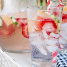 two glasses filled with ice and strawberries on a tray next to pitcher of water