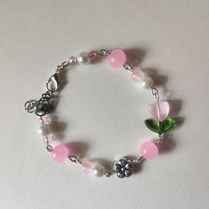 a pink and white bracelet with flowers, beads and charms on it's side