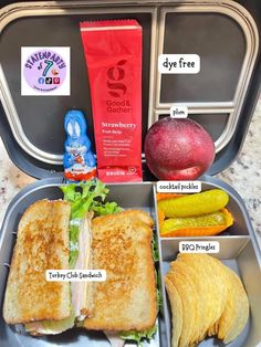 an open lunch box with sandwiches, chips and fruit