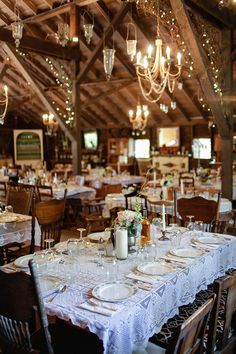 the tables are set with white plates and silverware for an elegant dinner in a rustic setting