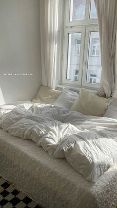 an unmade bed sitting in front of a window next to a checkered rug