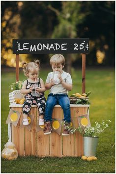 two young children sitting on top of a barrel with lemonade in front of them