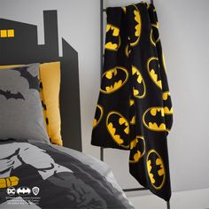 a batman themed bed spread with yellow and black accents on it, next to a gray headboard