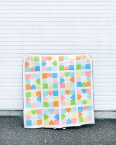 a multicolored quilt sitting on the ground next to a white wall with a garage door in the background