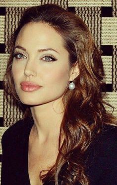 a woman with long brown hair and blue eyes posing for a photo in front of a wall