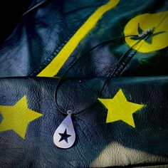 a black leather bag with yellow stars and a silver tear shaped pendant on the strap