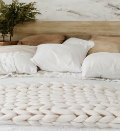 a bed with white blankets and pillows on it's headboard, next to a potted plant