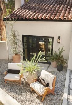 a patio with two chairs and a potted plant in front of the door to a house